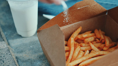 En person sitter och saltar en låda med pommes frites